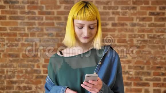 年轻迷人的女人黄发打电话微笑站在砖墙背景附近不寻常的人视频的预览图