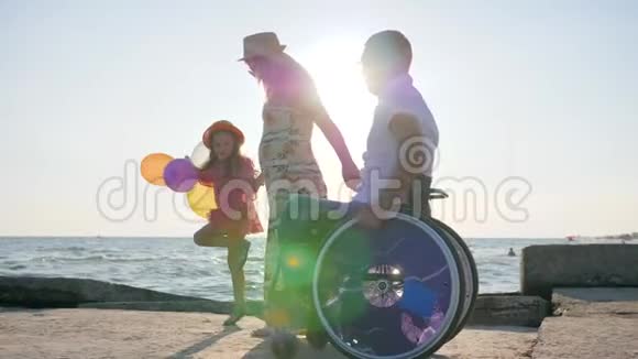和父母一起度假坐轮椅的快乐男人和妻子一起散步可爱的孩子拿着气球视频的预览图