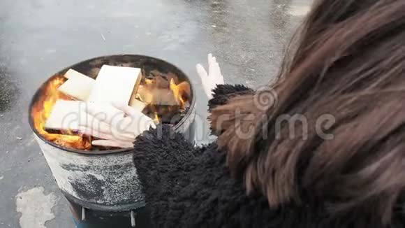 女人在燃烧的壁炉前搓手女孩正在温暖自己在冬天的火在一个圆桶视频的预览图