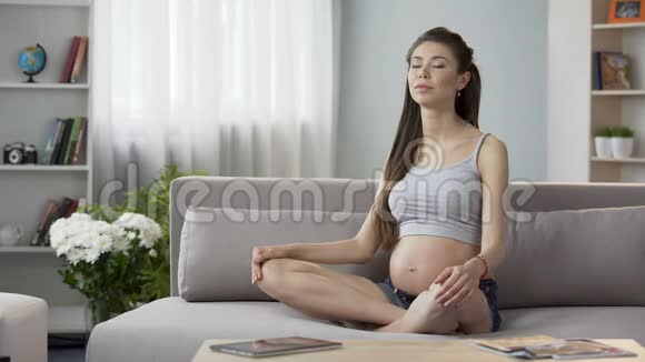 未来的母亲坐在沙发上沉思摸着肚子健康怀孕视频的预览图