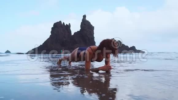 日落时美丽的运动女子在海滩上的木板位置的侧面景色视频的预览图