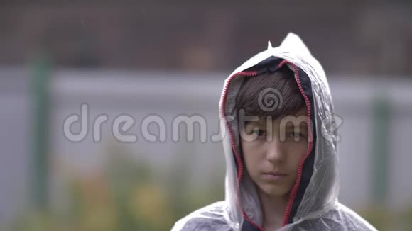悲伤的男孩站在雨中的雨衣里慢动作视频的预览图