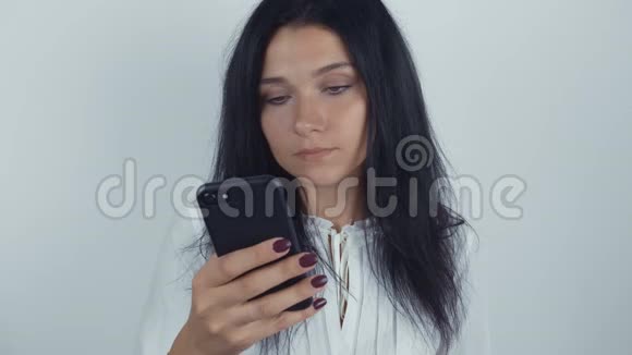 年轻女性黑发在白色背景下使用智能手机的肖像视频的预览图