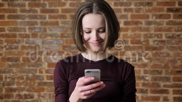 年轻漂亮的女孩正在智能手机上阅读信息微笑交流理念砖背景视频的预览图