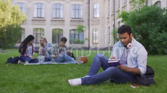严肃的混血男学生坐在草地上写论文做作业视频的预览图