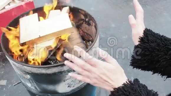 女人在燃烧的壁炉前搓手女孩正在温暖自己在冬天的火在一个圆桶视频的预览图