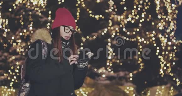 年轻漂亮的女人用智能手机在城市的夜晚手握户外微笑着脸上有灯光视频的预览图