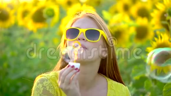 红长发的美女站在黄色的向日葵地上吹泡泡快乐的女人在户外青少年视频的预览图