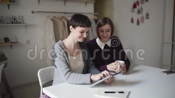 两个姐妹用平板电脑坐在家里的桌子上女人喜欢平板电脑视频的预览图