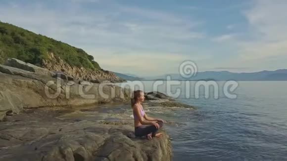 Flycam观景女孩坐瑜伽姿势对抗海潮到岩石视频的预览图