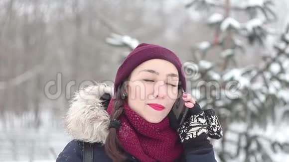 美丽的年轻女孩在冬天的公园里散步时在她的智能手机上说话视频的预览图