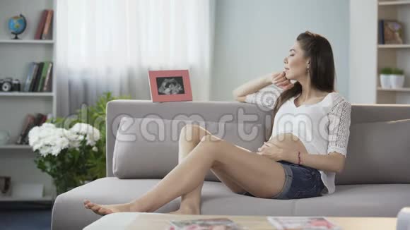 在沙发上期待的女士拿着镜框的超声波图看着它期待视频的预览图