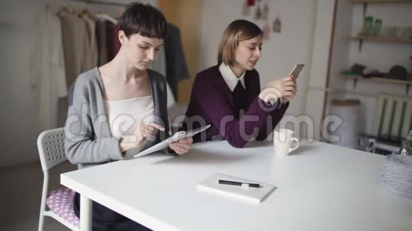 两名使用平板电脑和手机的女学生坐在桌子上视频的预览图