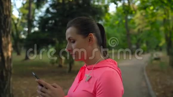 带着无线耳机和智能手机的女人选择音乐穿过秋天公园视频的预览图