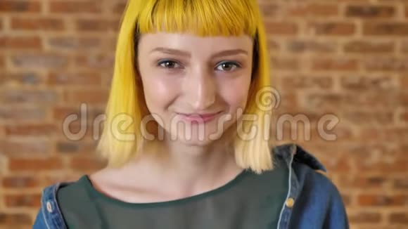 年轻美丽的女人的肖像黄色头发看着相机微笑砖墙背景快乐和视频的预览图
