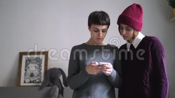 两个穿着时尚毛衣的女人在智能手机上看照片女性朋友八卦视频的预览图
