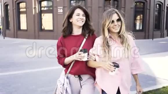 两个年轻女人拿着咖啡杯在夏天的大街上散步视频的预览图