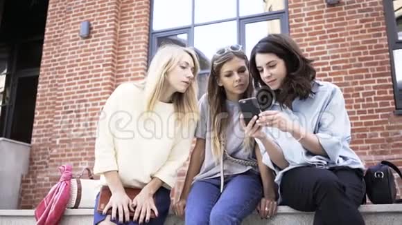 三个女人坐在夏季大街上看智能手机屏幕视频的预览图