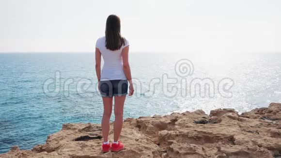 在阳光明媚的日子里女人缓慢地站在悬崖边免费女性看蓝色海景视频的预览图