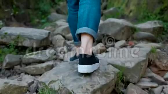 一个穿牛仔裤和交叉裤的女人的腿独自走在一条有很多石头的山路上视频的预览图