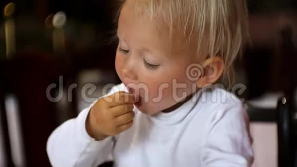 宝宝在餐馆吃东西坐在高脚椅上的金发碧眼的孩子从盘子里用手拿食物视频的预览图