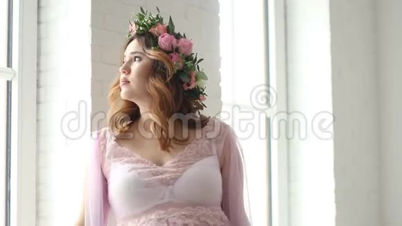 怀孕的女孩站在窗户附近穿着一件漂亮的粉红色连衣裙视频的预览图