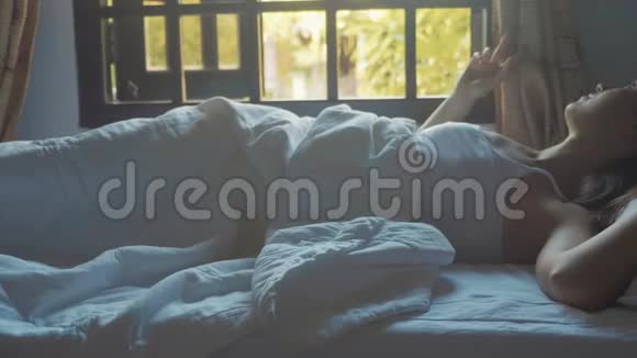 早上刚刚醒着的年轻女人躺在家里的床上的肖像视频的预览图
