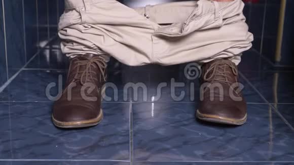 坐在马桶里肚子痛的人的脚4k特写穿着裤子和鞋子的男人视频的预览图