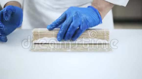 一位熟练的蓝手套厨师用竹席制作寿司视频的预览图