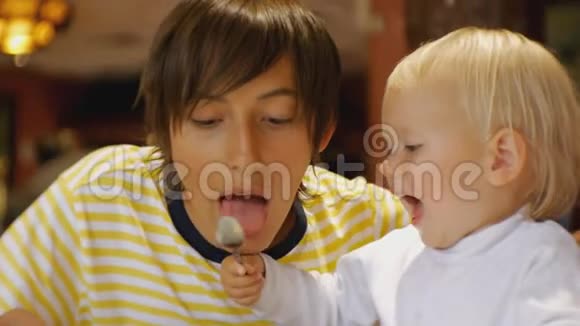 婴儿在餐馆吃食物开朗蓝眼睛的孩子笑着用勺子喂哥哥视频的预览图