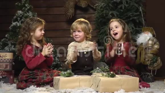 快乐的孩子们用新年的装饰拍手慢动作坐在礼物间视频的预览图