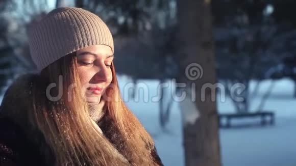 特写镜头一个年轻的女孩在风雪和阳光的映衬下用手吹着一堆雪视频的预览图