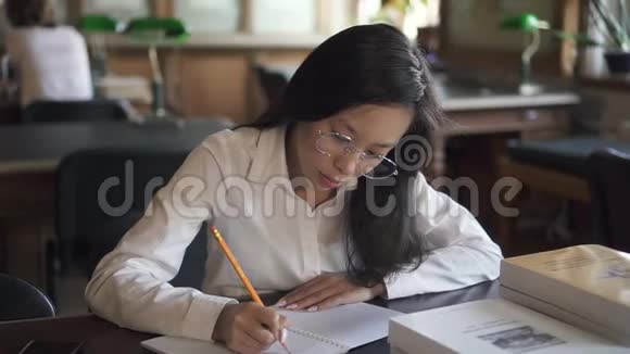 漂亮的女学生正坐在图书馆的桌子旁写字视频的预览图