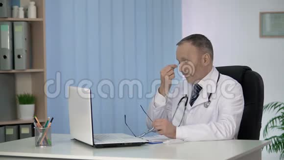 疲惫的男性治疗师在笔记本电脑上工作填写电子病历视频的预览图