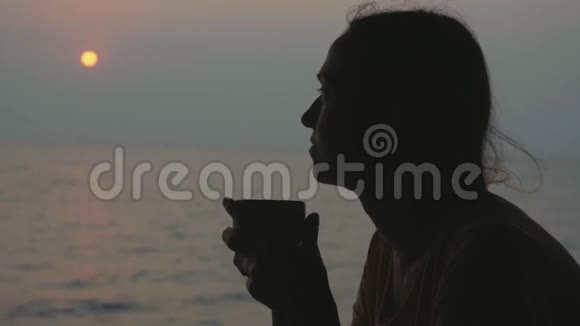 年轻女子坐在海景咖啡厅日落时分喝杯茶视频的预览图