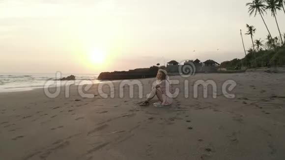 在日落时分穿着连衣裙戴着帽子在沙滩上放松视频的预览图