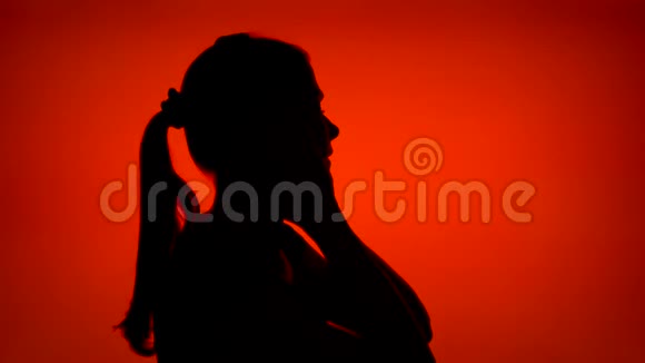 女人在红色背景上戴上耳机的剪影女性侧脸听音乐视频的预览图