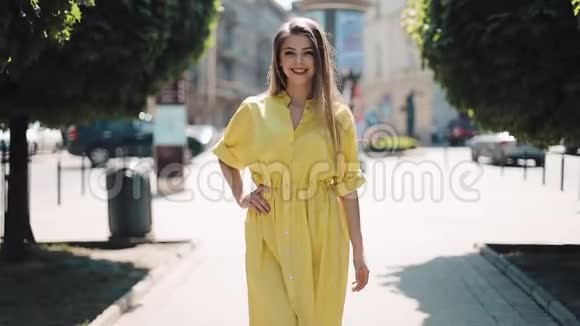 美丽的女孩穿着黄色的裙子沿着街道的城市走背景模糊阳光明媚的夏日阳光女子视频的预览图