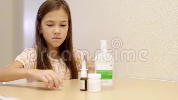 女孩用水摄取维生素和饮料小女孩坐在桌边喝药视频的预览图