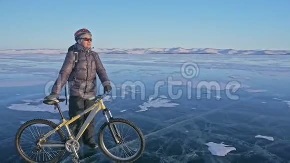人和他的自行车在冰上他站着看着美丽的日落骑自行车的人穿着灰色羽绒服视频的预览图