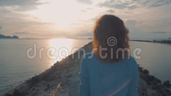 年轻的女孩走在海边走向日落越过肩膀稳健的射击视频的预览图
