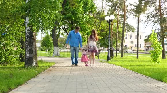 爸爸妈妈和宝宝一起玩举起手来小女孩蹦蹦跳跳地笑着夏天一家人在公园里散步视频的预览图