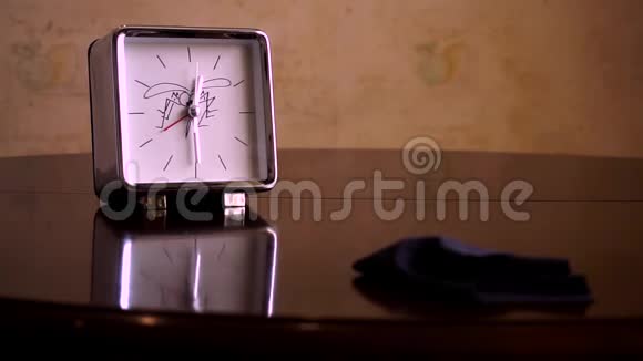在一张光滑的棕色木桌上有一个倒影有一个白色刻度盘的方形银一个有腿的钟a视频的预览图