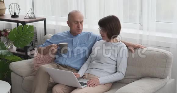 带笔记本电脑和沙发上的咖啡的老年夫妇视频的预览图