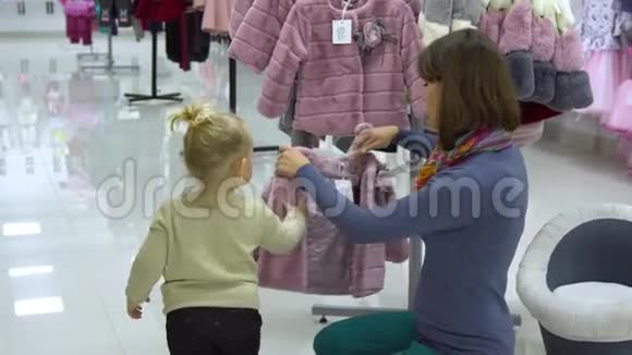 一个可爱的小女孩和她的母亲在一家精品店里家精品店妈妈和孩子在商店里挑选衣服视频的预览图