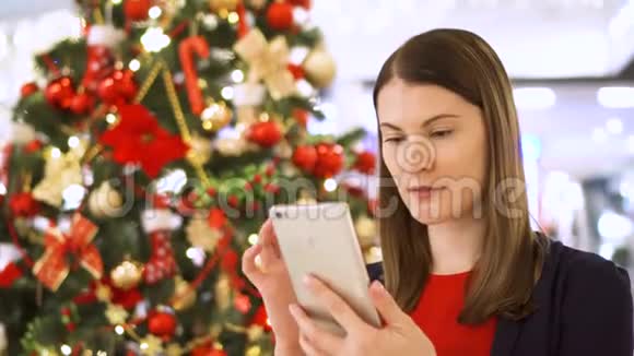 圣诞树附近的女人漂亮的女人用手机自拍做滑稽的脸视频的预览图