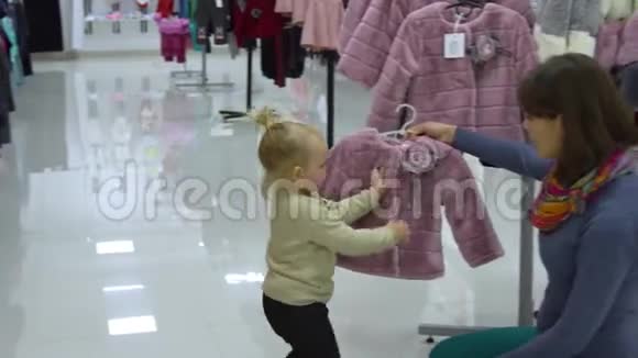 一个可爱的小女孩和她的母亲在一家精品店里家精品店妈妈和孩子在商店里挑选衣服视频的预览图