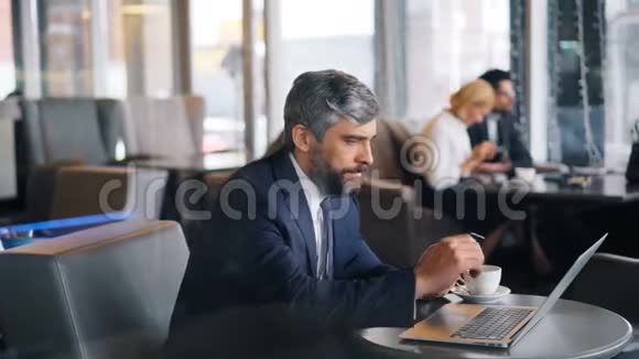 成熟的商人在咖啡馆的商务午餐中使用笔记本电脑和智能手机视频的预览图