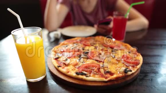 嬉皮士女孩在咖啡馆里用智能手机前台有意大利披萨和果汁视频的预览图