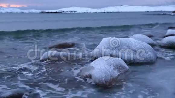 日落时分巴伦支海岸边的波浪和冰石视频的预览图